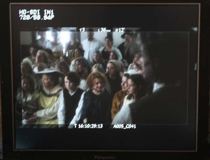 The view on the camera monitor over Malcolm Stiles' (Macleish Day) shoulder to Lady Catherine (Christa Cannon) and young Henry Stiles (Tom Place) 
in the crowded courtroom.